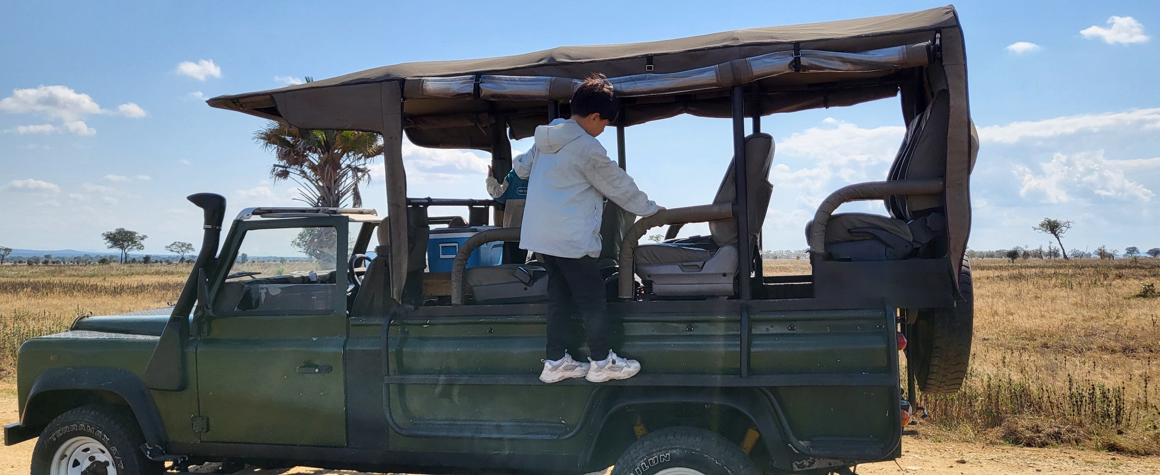 A boy climbing onto a green open-sided safari Land Rover in Mikumi National Park