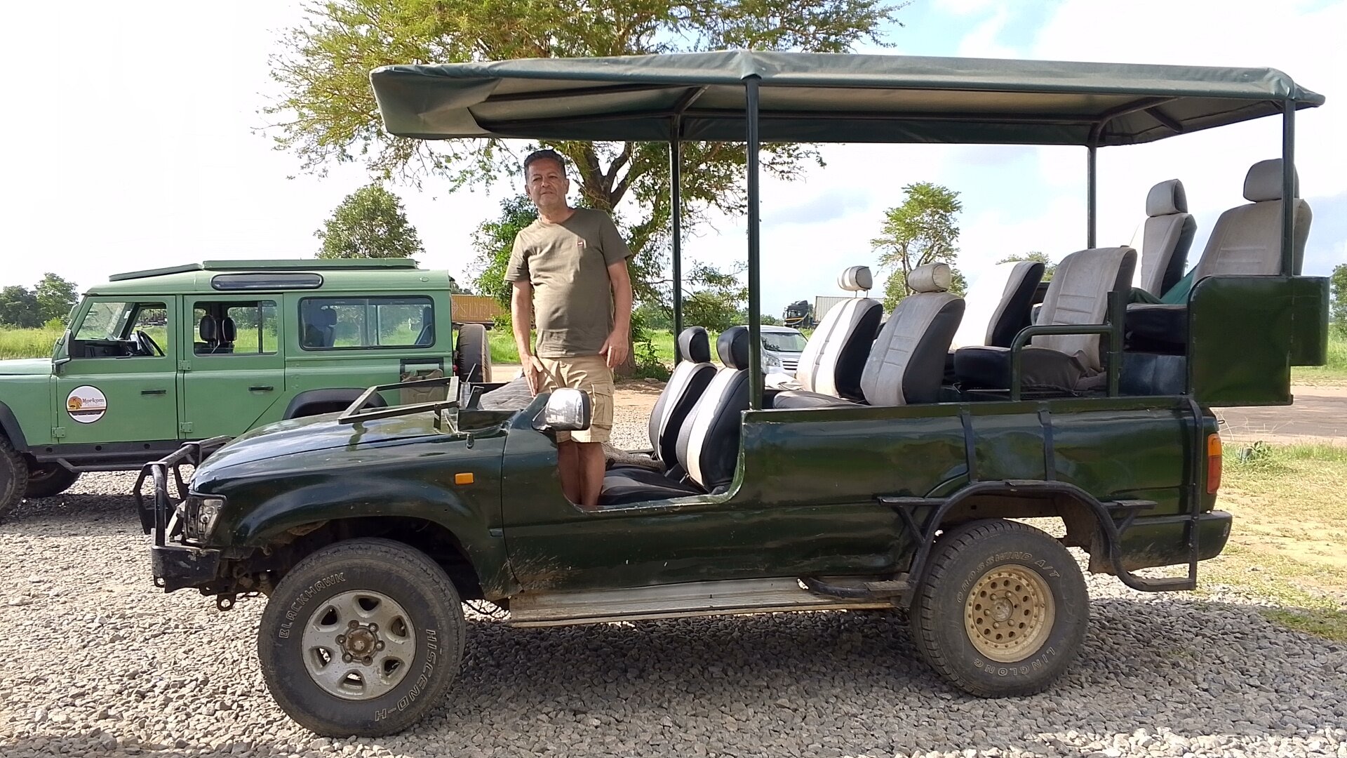 Guide beside an open sided green safari truck on gravel in Mikumi
