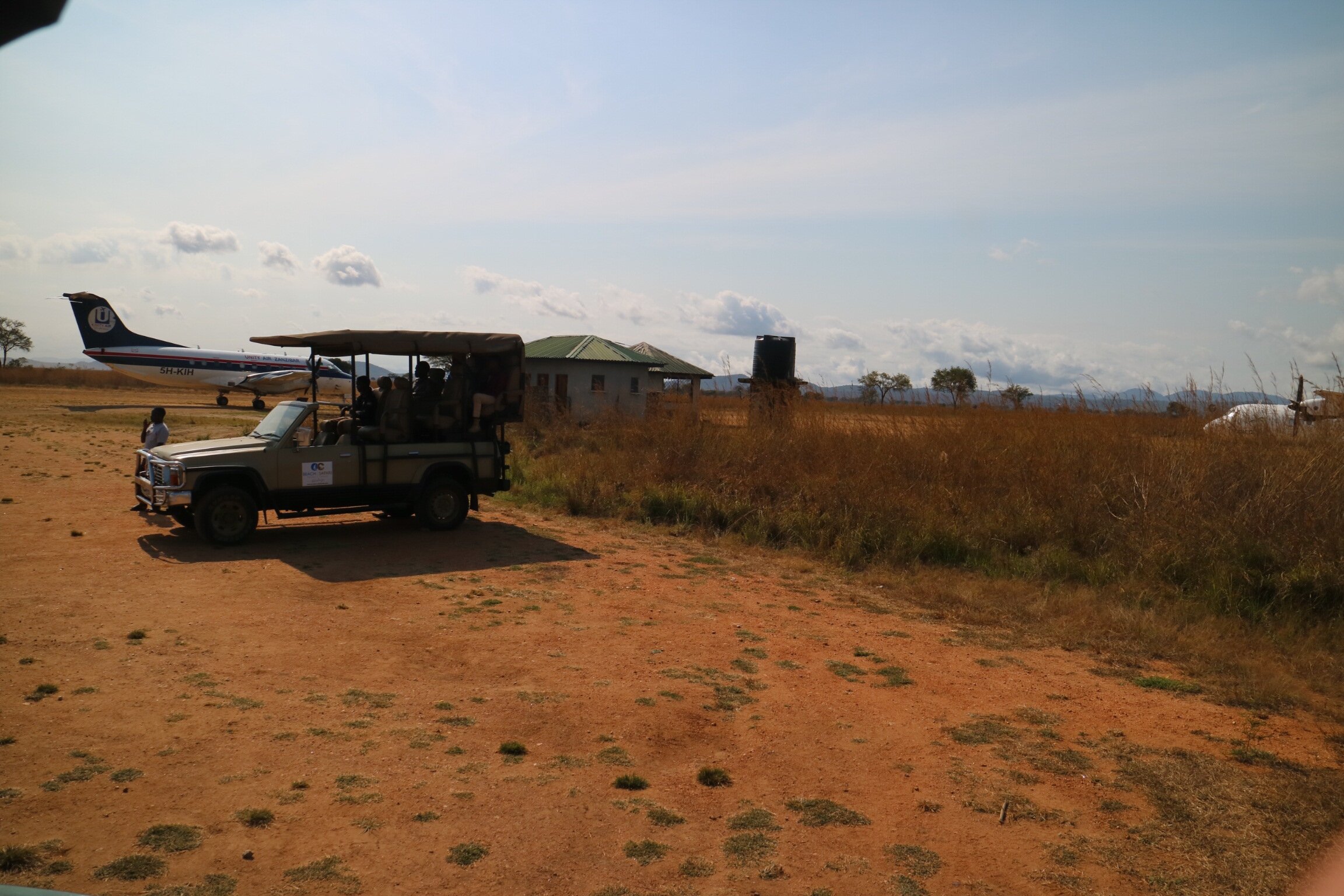 Safari vehicle with guests beside the airstrip and plane in Mikumi