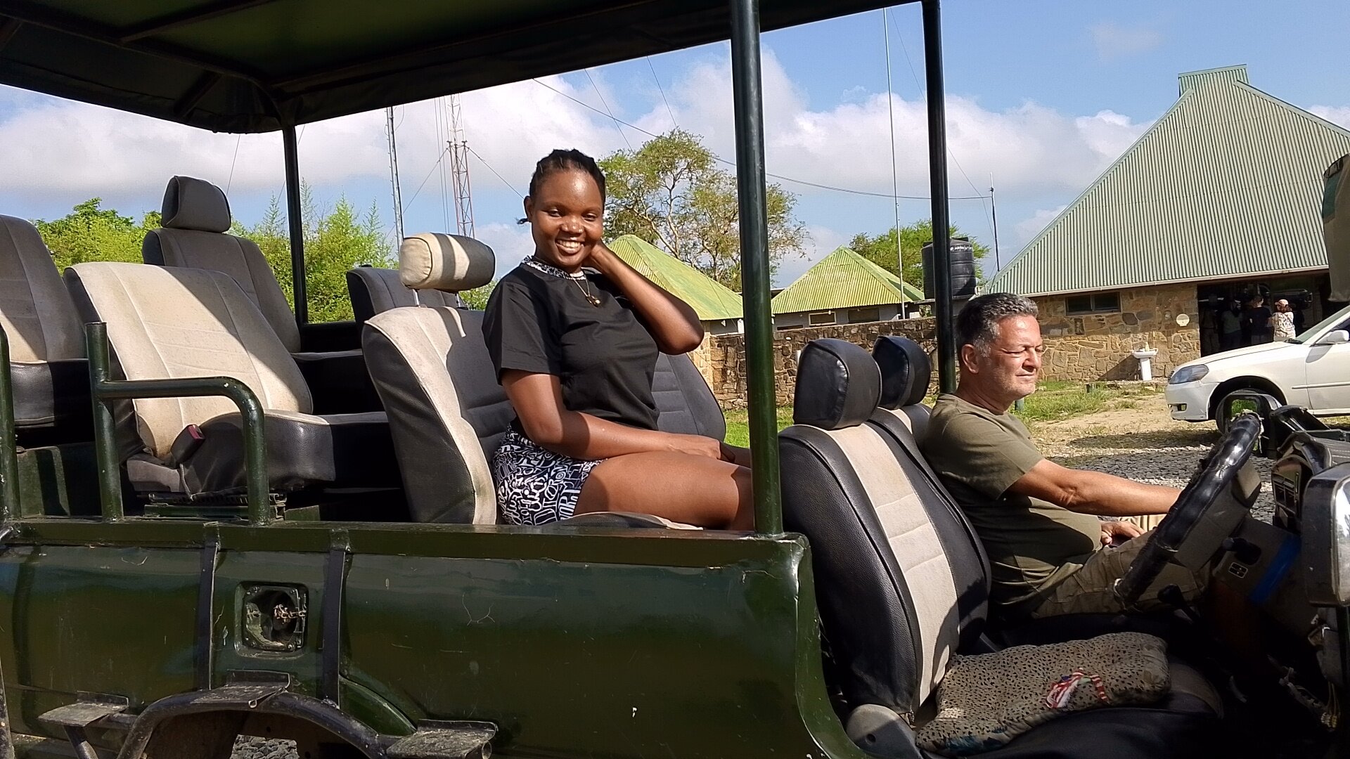 A smiling guest and driver in an open safari truck at Mikumi park buildings