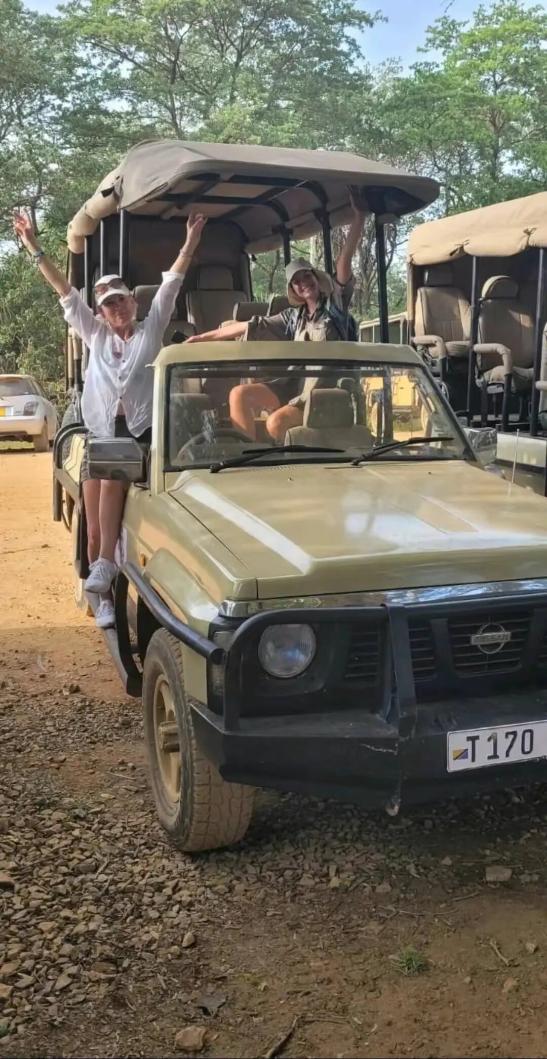 Two guests waving from a cream open safari vehicle in Mikumi